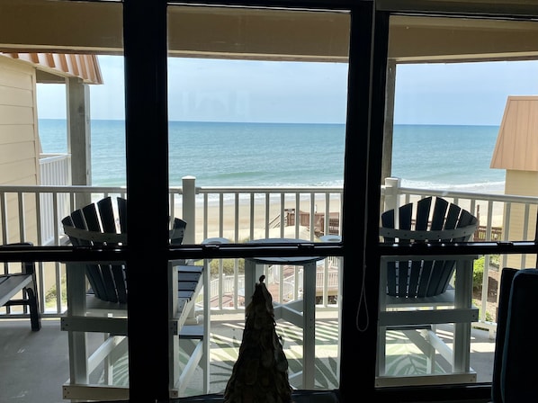A balcony with two Adirondack chairs, a view of the ocean, and a beach in the background.