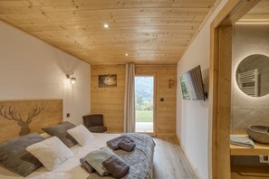 A wooden-paneled room with a bed, a chair, a television, and a view of the outdoors.