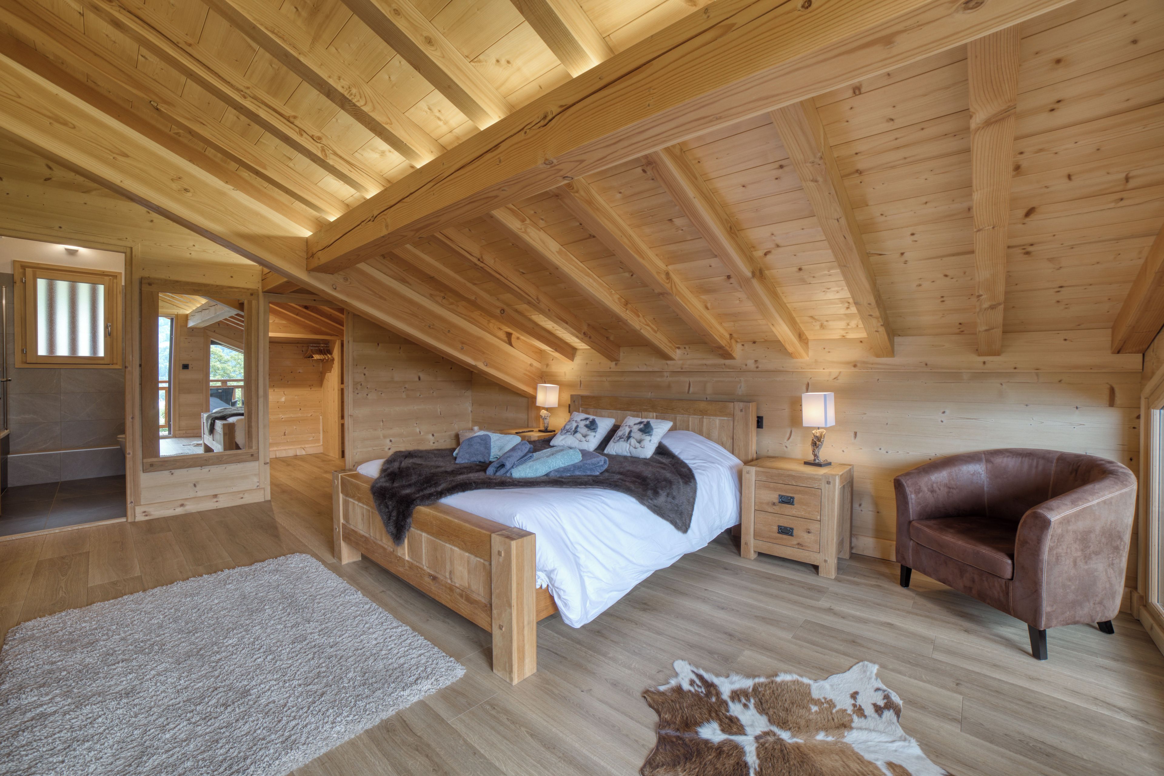 A wooden cabin bedroom with a bed, nightstands, a leather chair, and a rug.