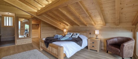 Une chambre dans une cabane en bois, avec un lit, des tables de chevet, un fauteuil en cuir et un tapis.