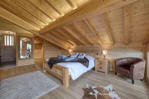 Ein Schlafzimmer einer Holzhütte mit einem Bett, Nachttischen, einem Ledersessel und einem Teppich.