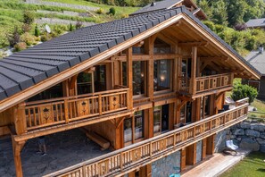 Eine zweistöckige Holzhütte mit geneigtem Dach, großen Fenstern und einem Steinfundament.
