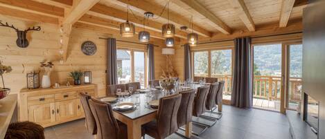 Een houten eetkamer met een lange tafel gedekt voor een maaltijd, grote ramen en uitzicht op het landschap.