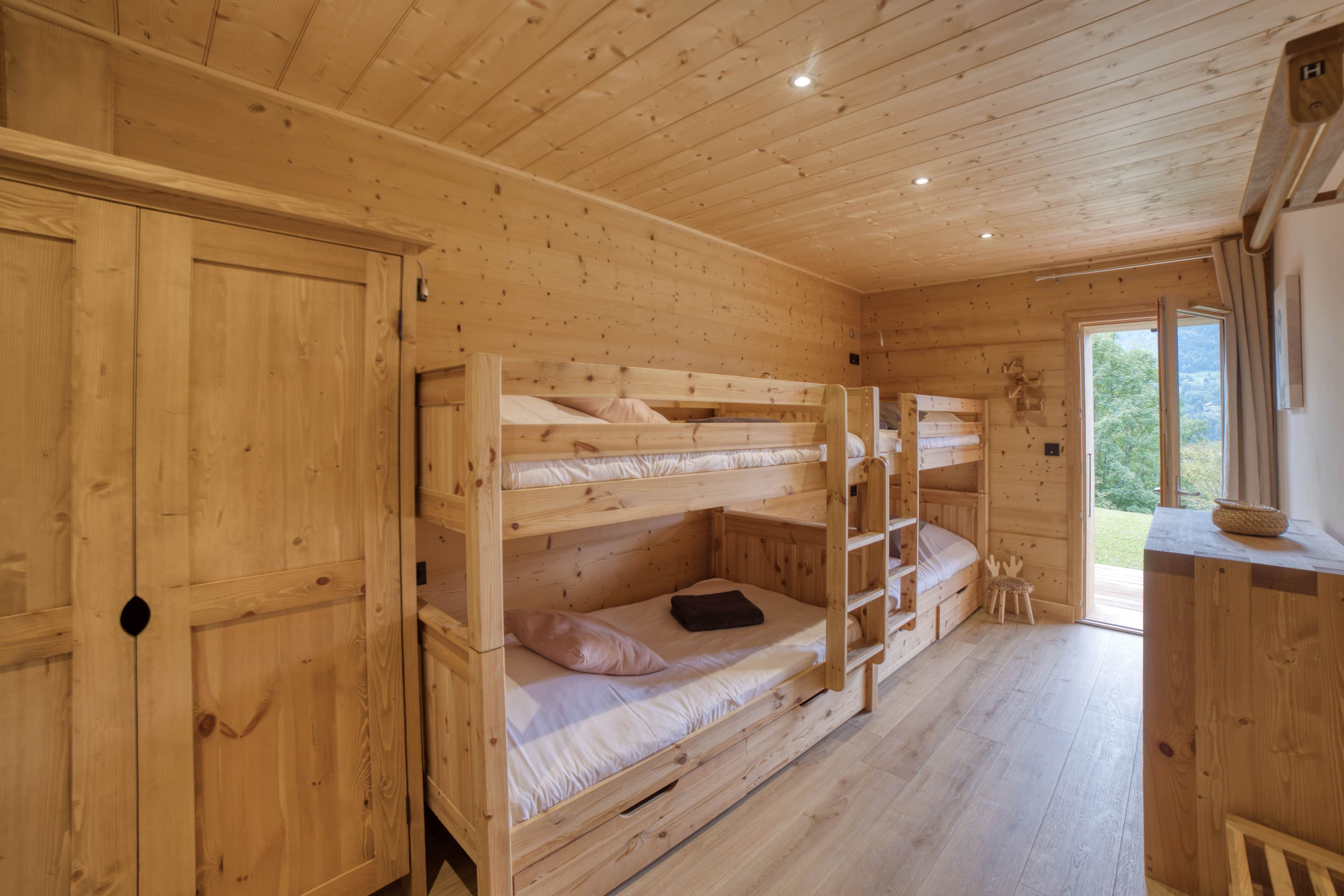 Een houten hut met stapelbedden, een garderobe en een eettafeltje.