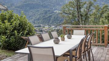 An outdoor dining area with a table and chairs, surrounded by a wooden deck and a view of a mountainous landscape.
