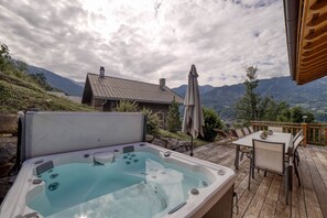 Un bain à remous sur une terrasse en bois avec vue sur les montagnes, une table avec des chaises et un parasol.
