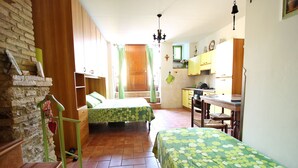 A compact room with two beds, a wooden staircase, a kitchen area, and a brick wall.