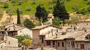 A historic stone building with a tower, surrounded by lush greenery and traditional houses.