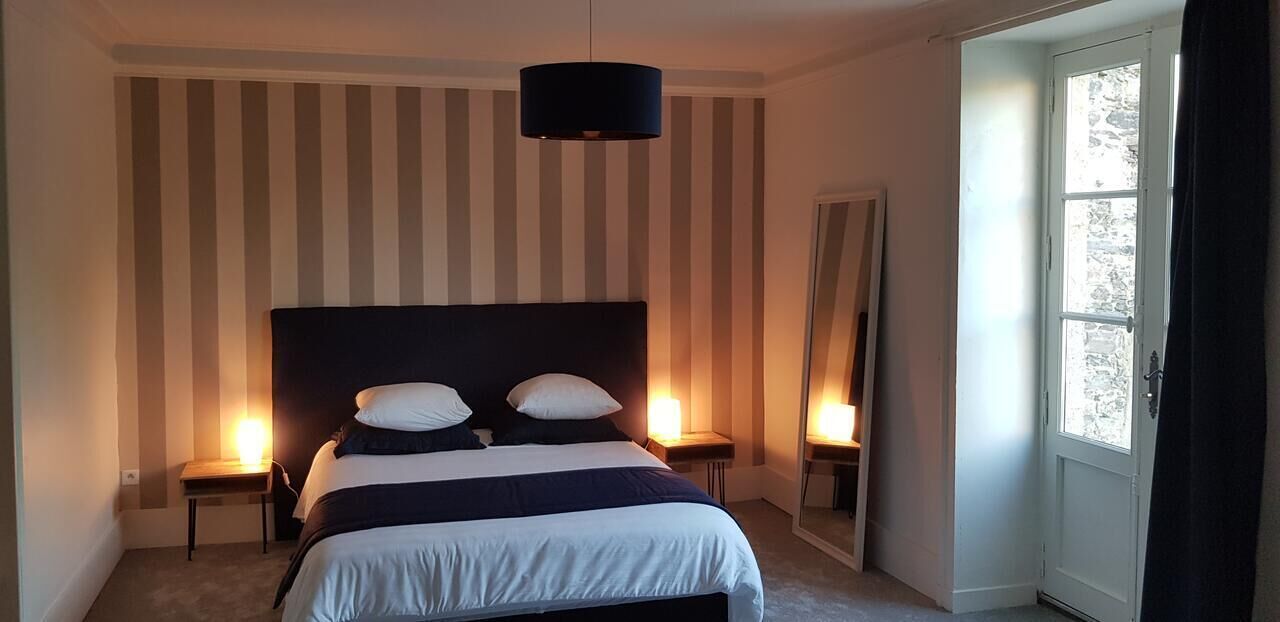 Une chambre à coucher avec un grand lit, un papier peint à rayures, deux tables de chevet avec des lampes et une fenêtre avec des rideaux.