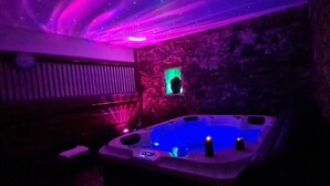 Een wellnessruimte met een stenen muur, een jacuzzi en paars licht.