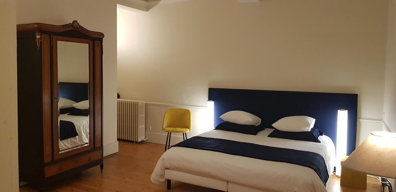 Een slaapkamer met een bed, een spiegel, een stoel en een lamp.