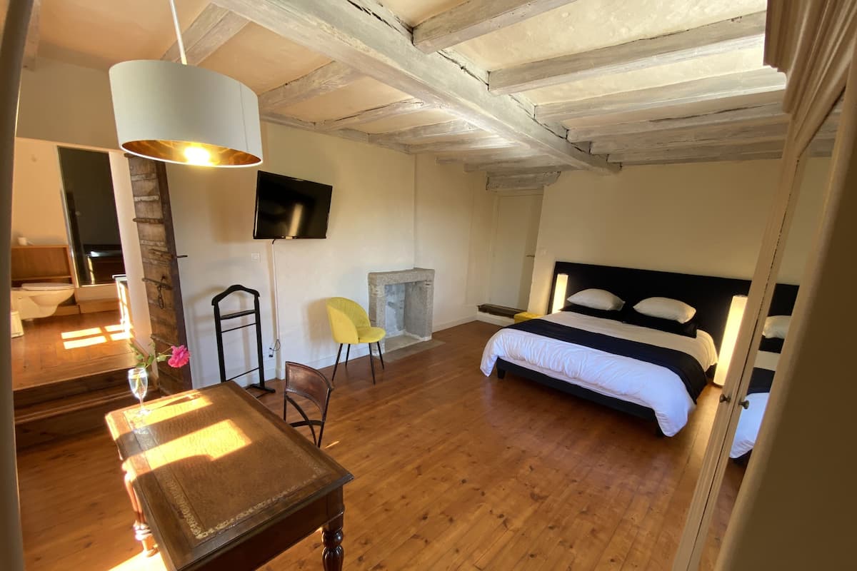 Un dormitorio con cama, televisor, chimenea, piso de madera y comedor con mesa y sillas.