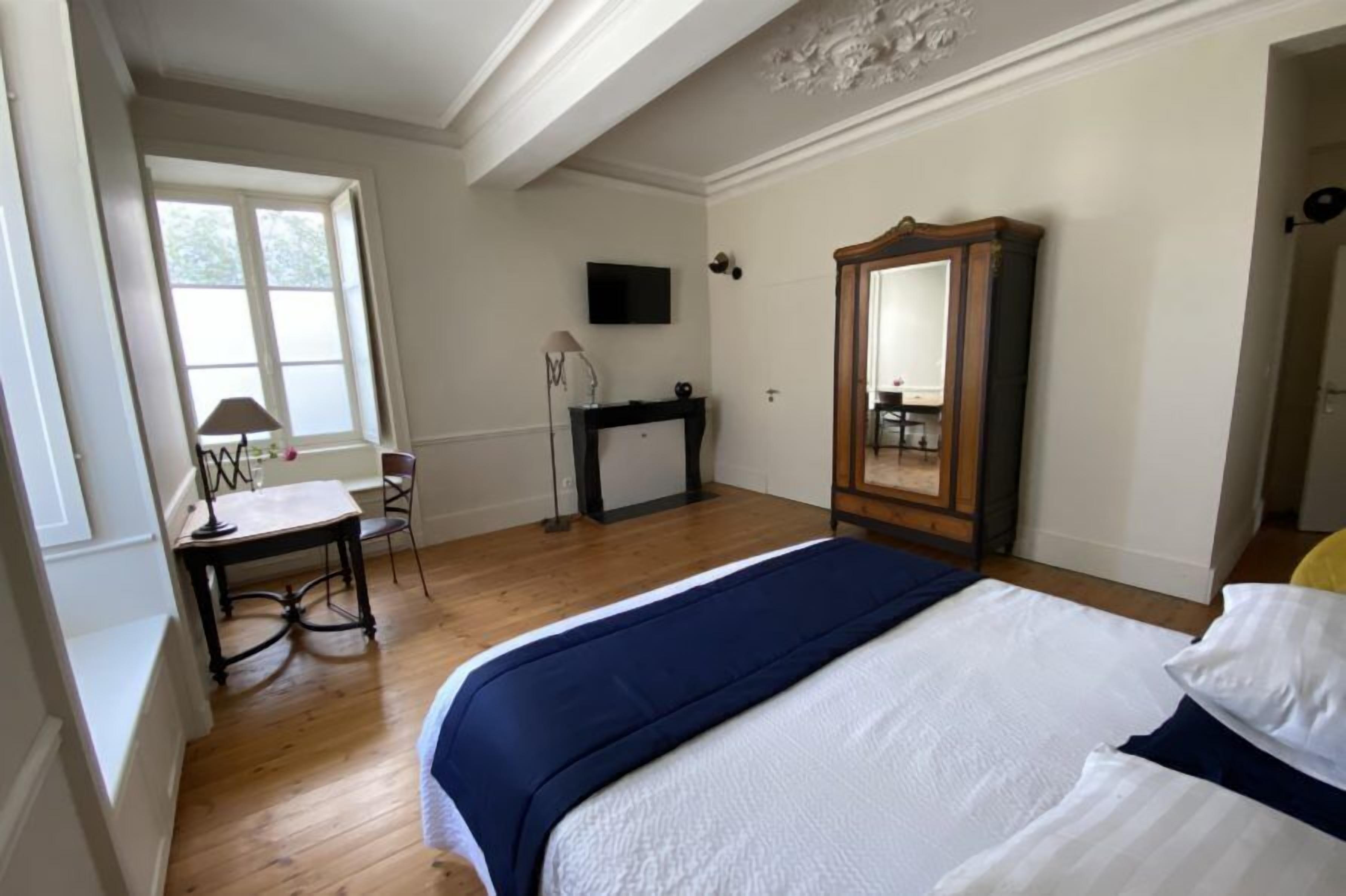 A bedroom with a bed, a desk, a chair, a television, and a mirror.