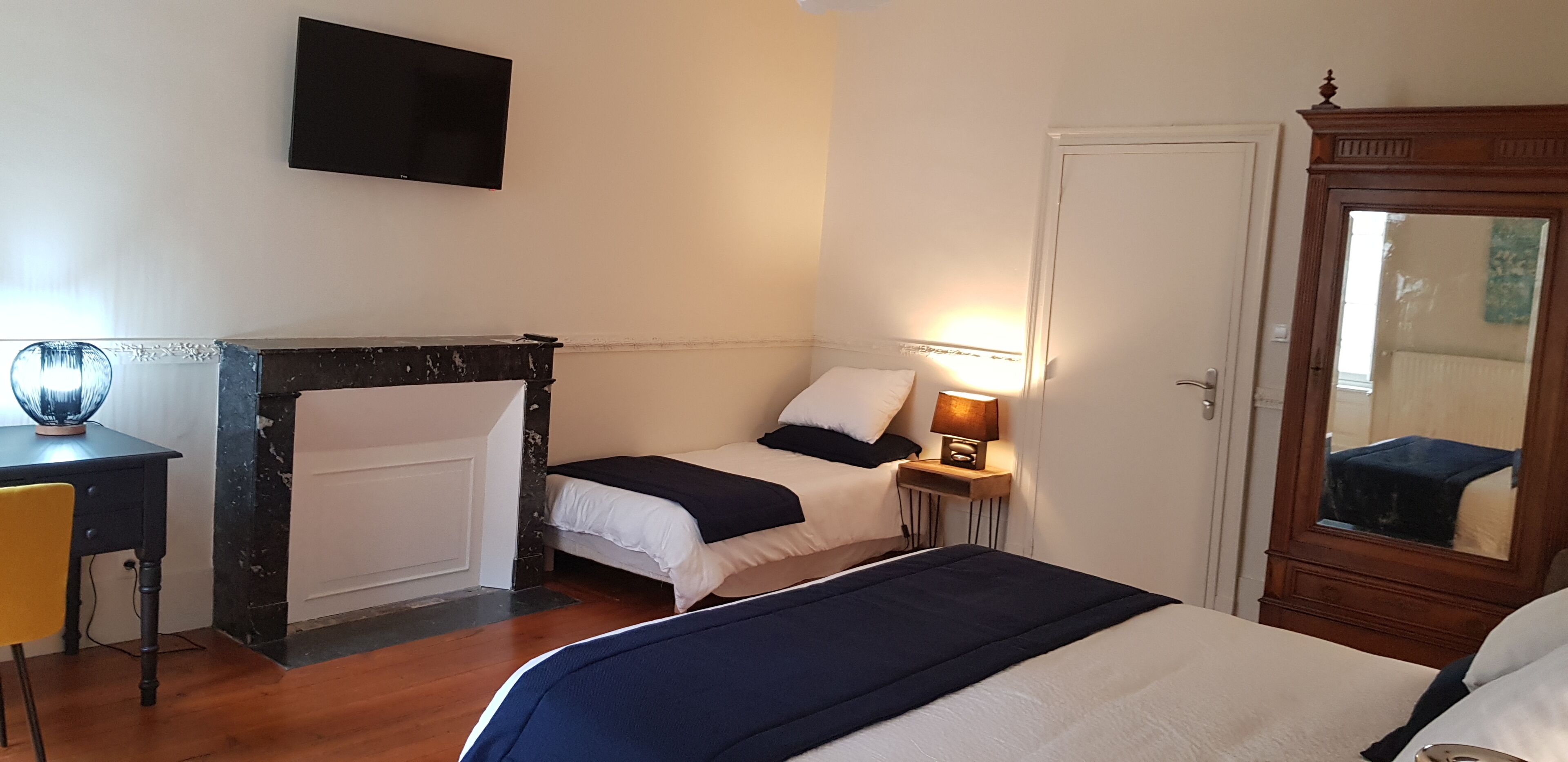 A hotel room with a bed, bedside table, lamp, TV, and a mirror.