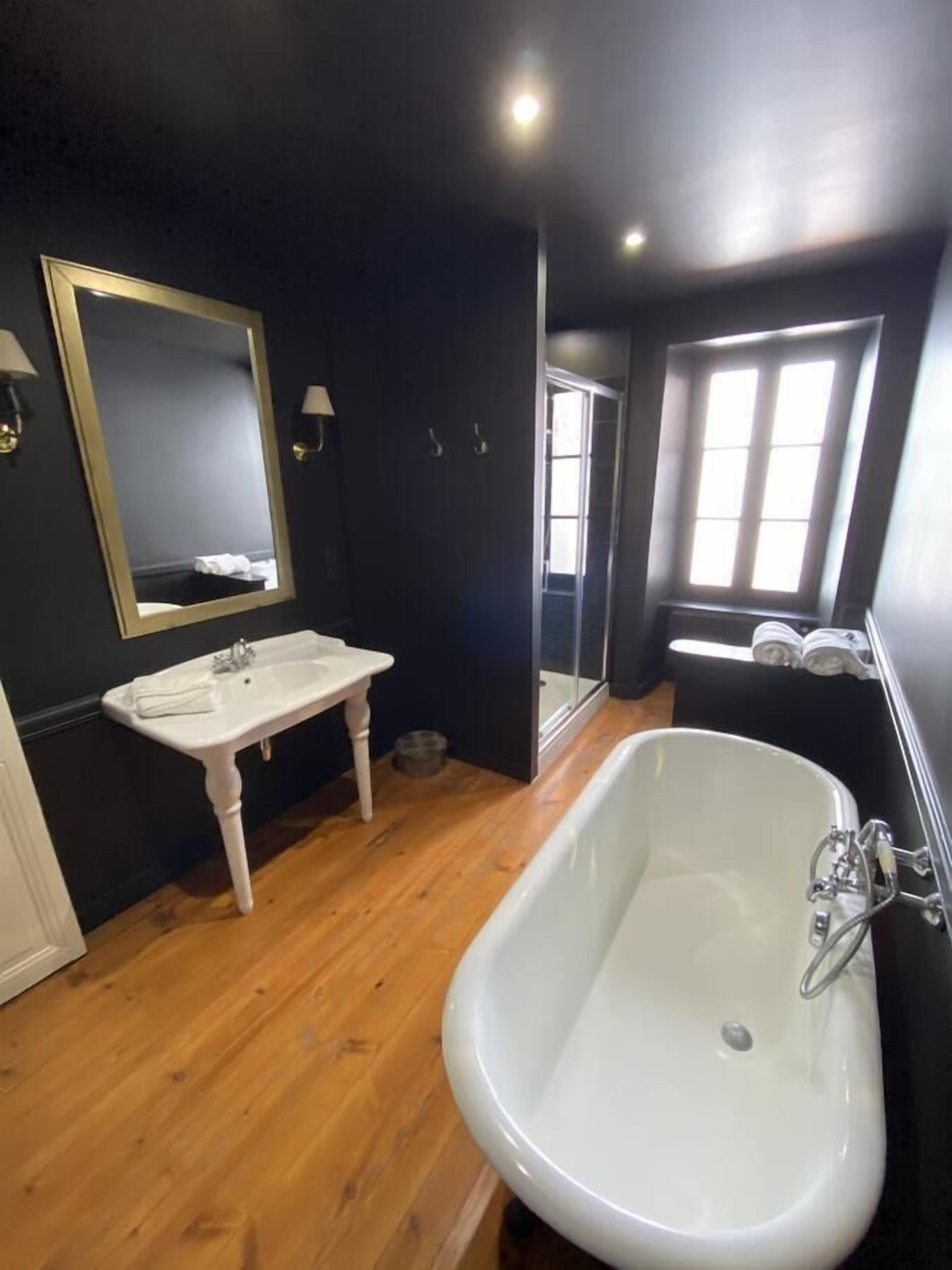 A bathroom with a white sink, a large mirror, and a freestanding bathtub.