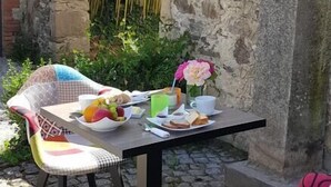 Een terras met een stenen muur, bamboeplanten en een gedekte tafel met een schaal fruit, een bloevas en een beker.