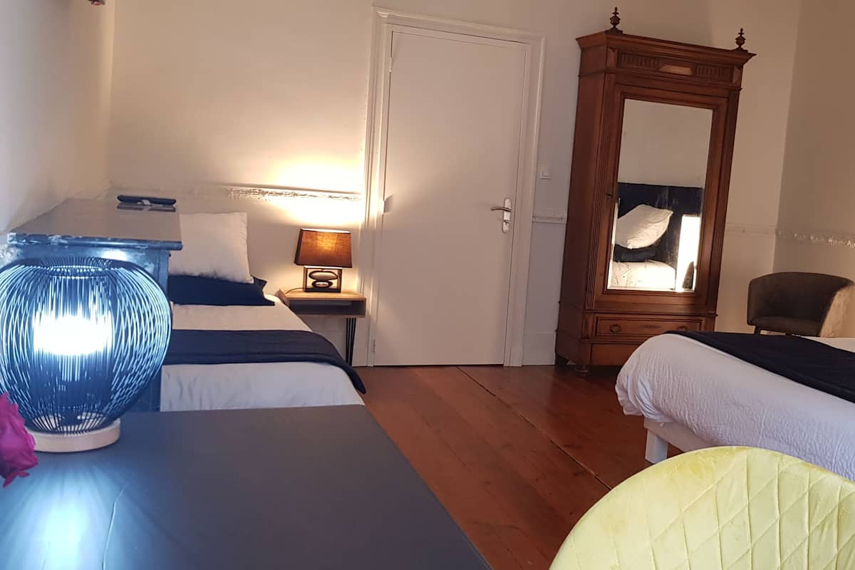 Habitación de hotel con dos camas, un armario de madera, una silla y una mesita de noche con lámpara.