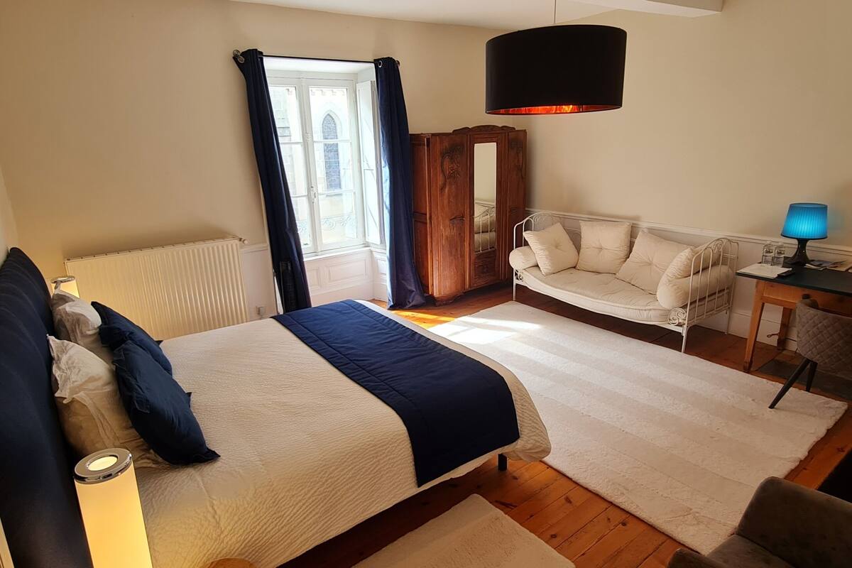 Un dormitorio con cama, escritorio, silla, sofá, televisión y ventana con cortinas.