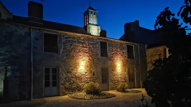 Een gebouw van steen met een klokkentoren aan het einde, verlicht door warme lichten.