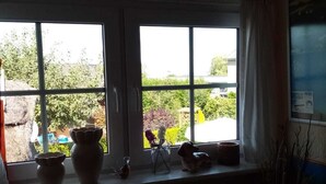 A room with a window overlooking a garden. There are two windows, a vase, and a small figurine on the windowsill.