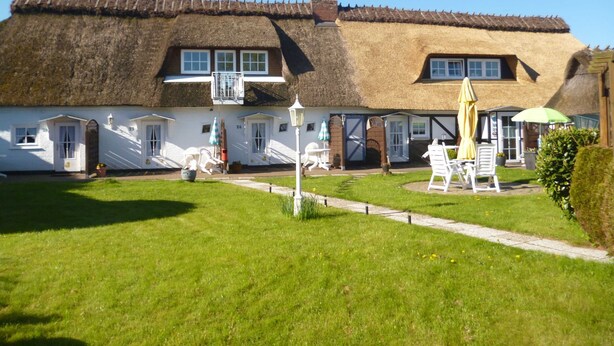 A thatched-roof building with a garden area, outdoor seating, and a pathway leading to the entrance.