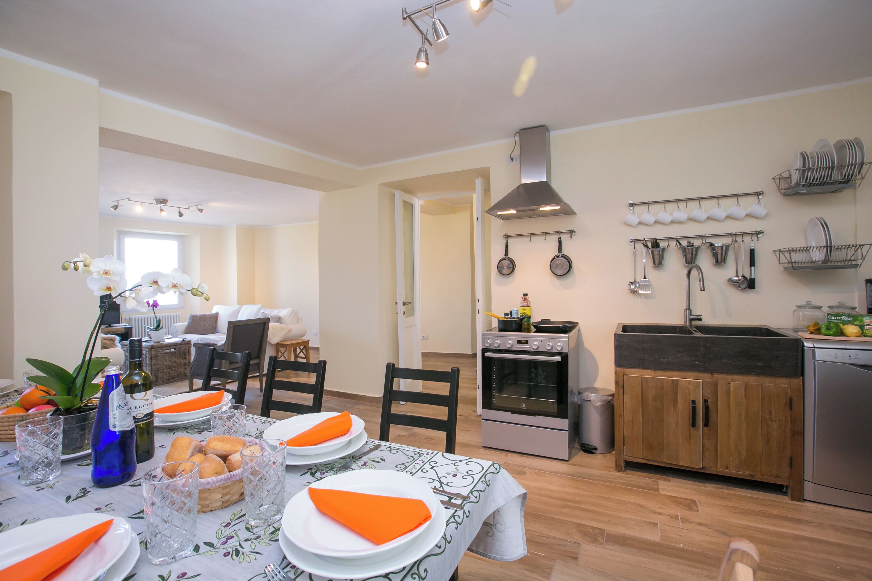 A dining area with a table set for four, kitchen appliances, and a dining table with orange napkins.