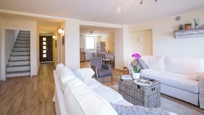 Una sala de estar con un sofá, un sillón y una mesa de centro con una cesta. Se ve una escalera al fondo.