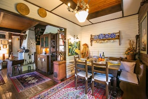 A cozy dining area with a wooden table, chairs, and a rug. There is a chandelier above the table and a shelf with decorative plates. - Argegno Chalet (Schignano)
