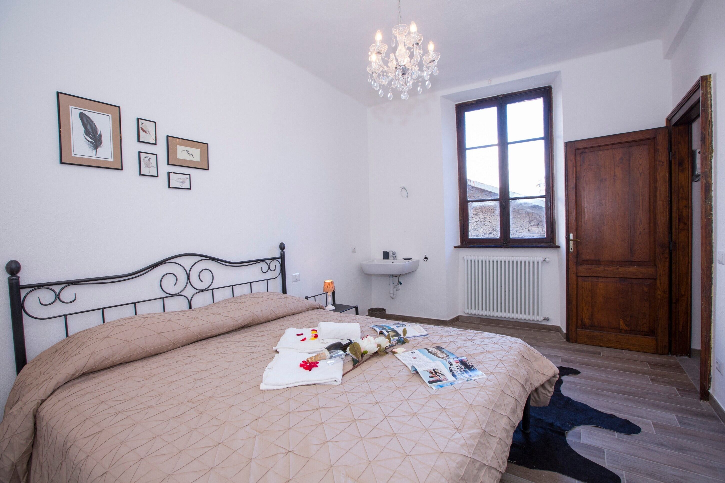 Una camera da letto con un letto, un lampadario, una finestra, una porta in legno e quadri appesi alle pareti.