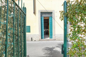A narrow street with a building entrance featuring a metal gate and a door with blue shutters. - Casetta al Lago (Tremezzina)