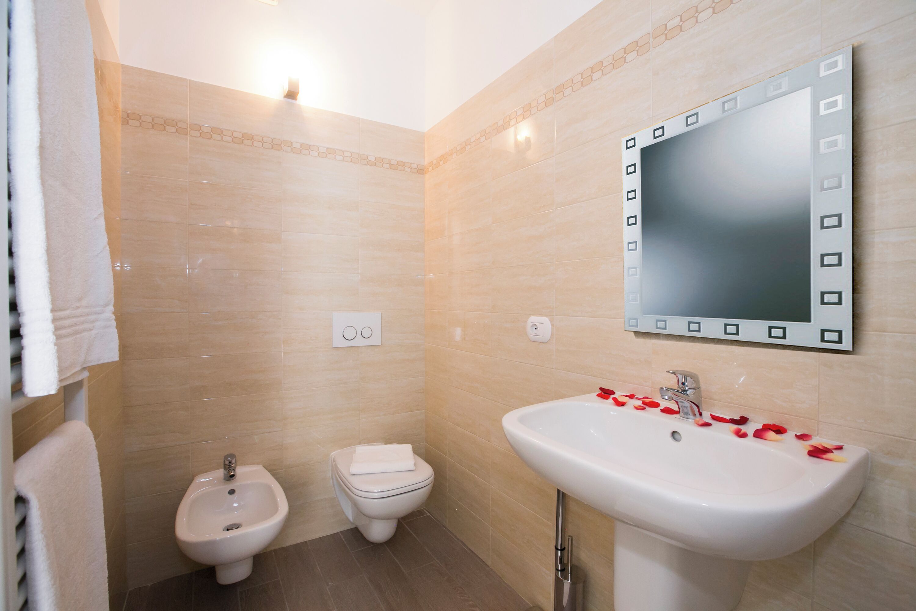 Un baño con bidé, inodoro, lavabo y un espejo con marco decorativo.