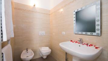 Un baño con bidé, inodoro, lavabo y un espejo con marco decorativo.