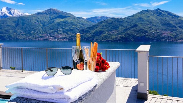 A poolside area with a view of mountains, a bottle of champagne, glasses, a bouquet of red roses, and a stack of towels. - Casa Laura Apt. 6 (Menaggio)