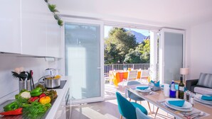 A modern kitchen with a dining area, a balcony with outdoor seating, and a view of trees and mountains. - Casa Laura Apt. 6 (Menaggio)