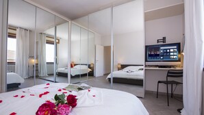 Hotellihuone, jossa on suuri sänky, työpöytä, tuoli, televisio ja peili.