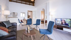 A spacious living room with a high ceiling, a television, and a dining area with blue chairs.