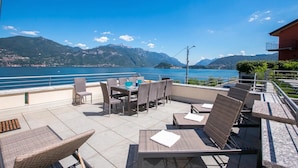 Terraço ao ar livre com móveis de vime e vista para um lago e montanhas.