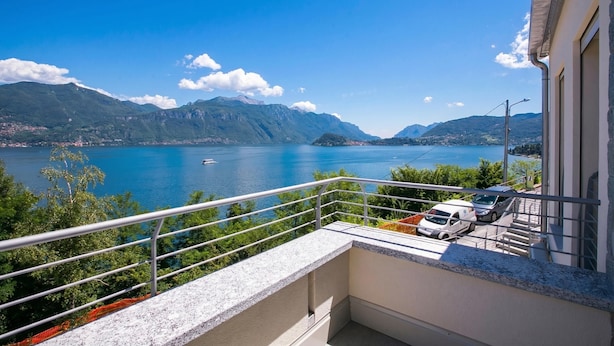Un balcon donnant sur un lac et des montagnes, une voiture garée à l’intérieur, et un bâtiment à la façade blanche.