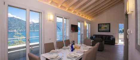 Comedor con mesa preparada para seis comensales, ventanas amplias y vista al mar.