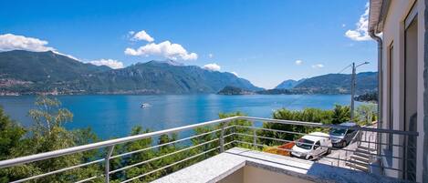 A balcony with a view of a lake and mountains, a car parked inside, and a building with a white facade.