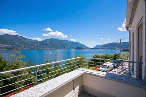A balcony with a view of a lake and mountains, a car parked inside, and a building with a white facade. - Paradiso di Menaggio Penthouse (Menaggio)