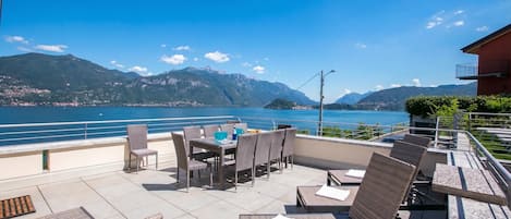 Een terras buiten met rieten meubilair en uitzicht op een meer en bergen.