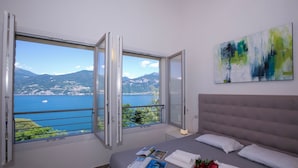 Um quarto com uma cama, janela com vista para um lago e montanhas, e um quadro na parede.