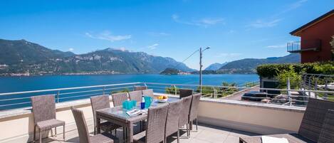 A terrace with wicker furniture, a table with drinks, and a view of a lake and mountains.