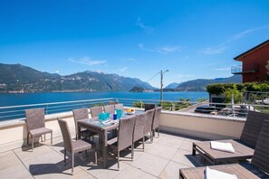 A terrace with wicker furniture, a table with drinks, and a view of a lake and mountains. - Paradiso di Menaggio Penthouse (Menaggio)