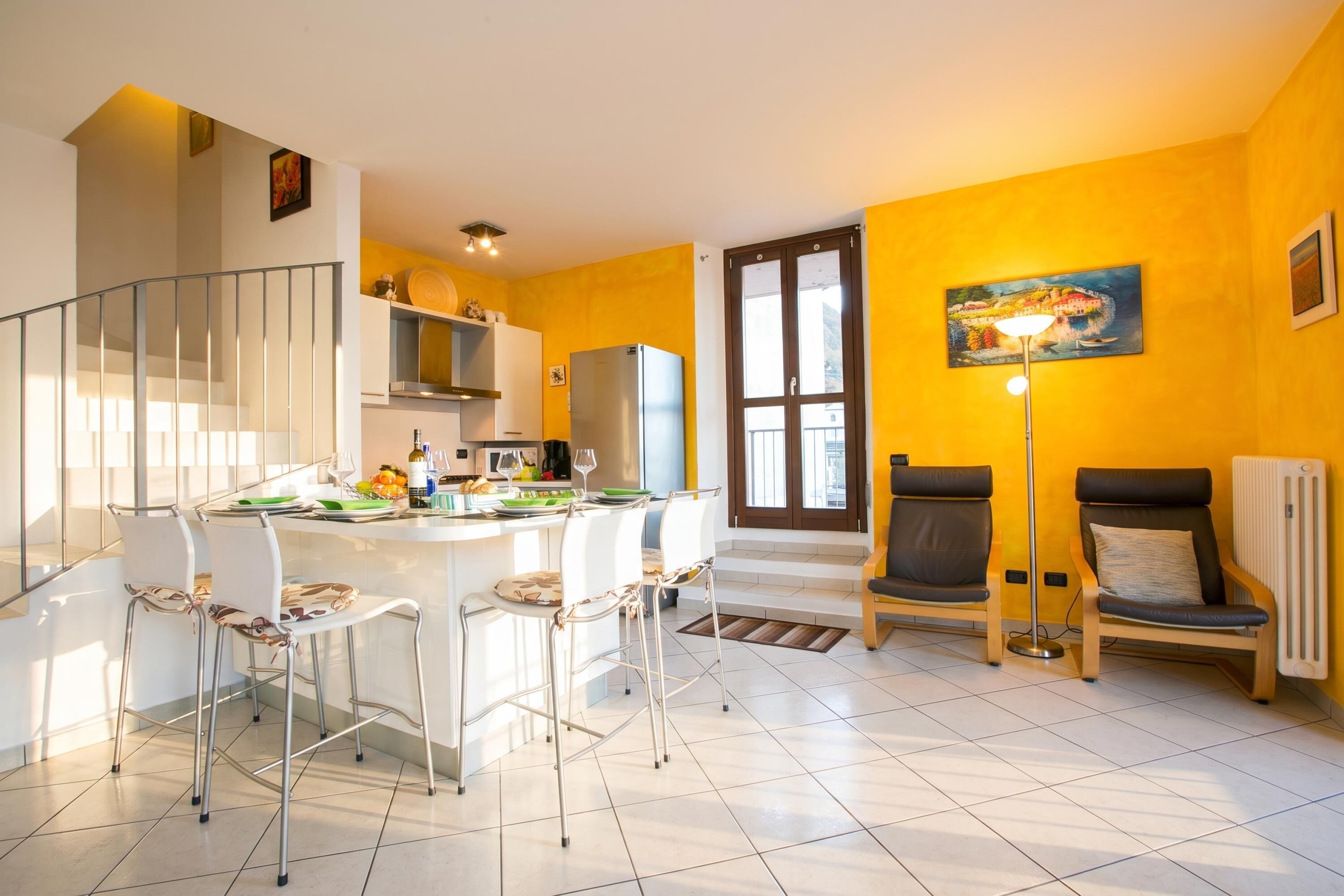 A modern kitchen with white cabinets, a dining area with white chairs, and a yellow wall.