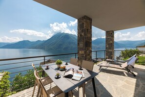 An outdoor terrace with a table set for dining, stone pillars, and a view of a lake and mountains.