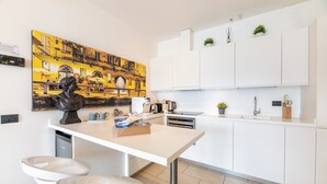 Een moderne keuken met witte kasten, een eettafel en een groot stadsgezichtschilderij aan de muur.