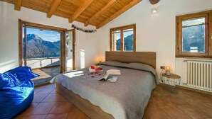 Ein Schlafzimmer mit einem Bett, einem blauen Sitzsack, einem Nachttisch mit Lampe und Blick auf Berge durch große Fenster.