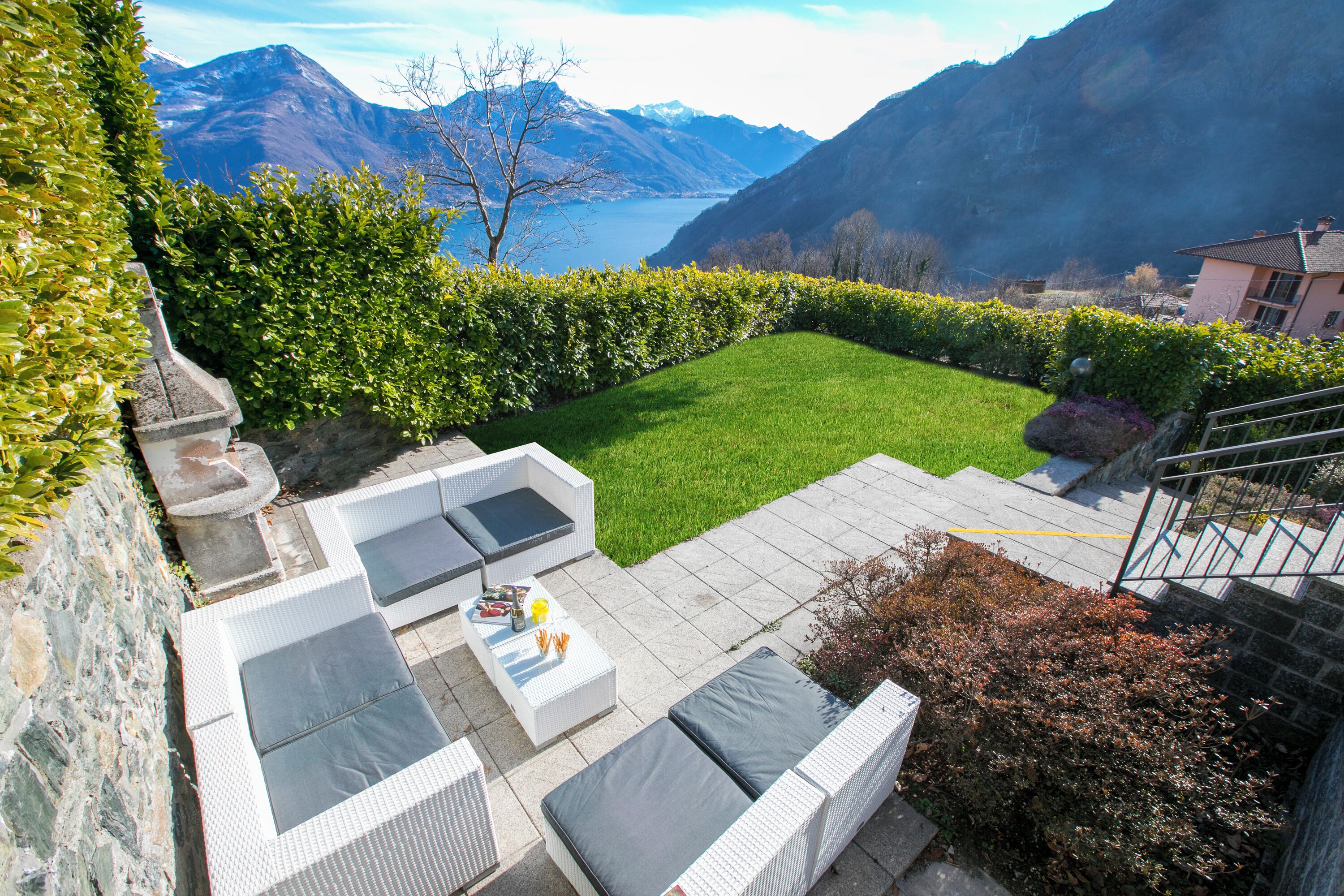 A patio with outdoor furniture, a grassy lawn, and a view of mountains and a lake.